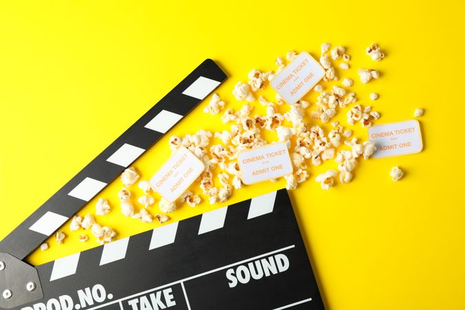 Flat lay composition with clapperboard, popcorn and tickets on yellow background