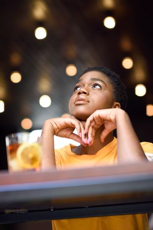 Female deep in thought sitting with ice tea at counter of modern cafe