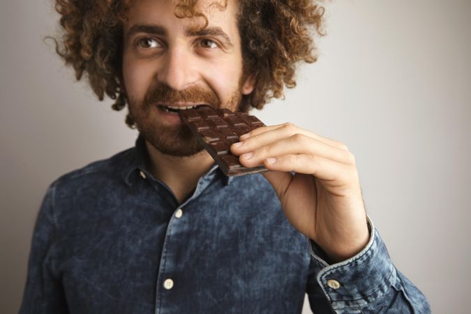 Man with curly hair biting into chocolate bar