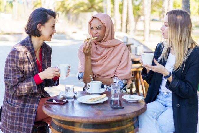 Three happy women chatting over coffee and baked goods on sunny outside table
