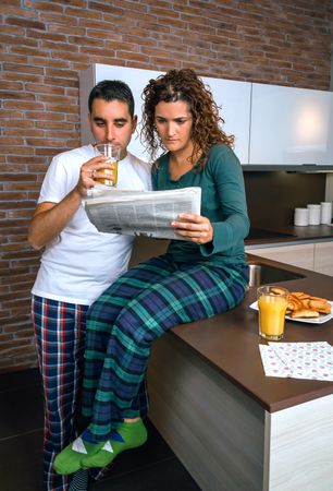 Couple in pajamas reading paper together in kitchen at breakfast