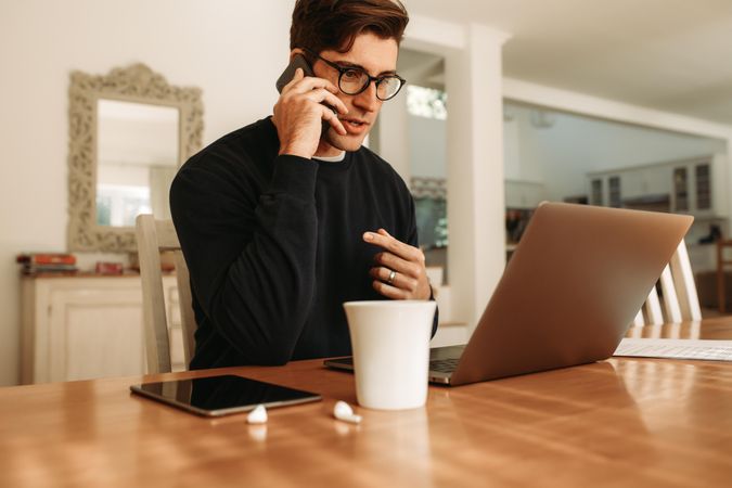Businessman at home working on laptop and talking over mobile phone