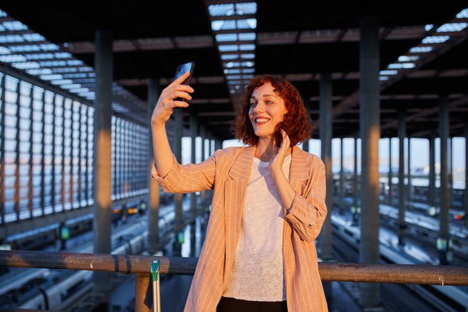 Smiling young woman taking selfie at station