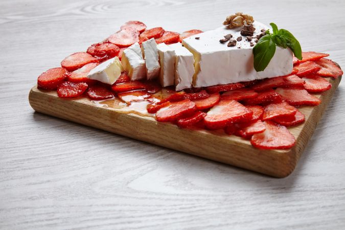Large slice of cheese and sliced strawberries on wooden board