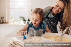 Young girl scooping baking ingredients into bowl with mom bG7lXb