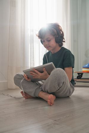 Focused preteen boy using tablet on floor in room