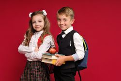 Preteens in school uniform carry backpacks on vivid red colored background