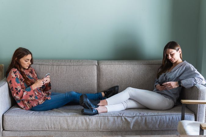 Young women resting on sofa and browsing smartphones