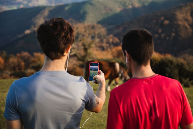 Men taking picture with mobile phone of mountain landscape and cow
