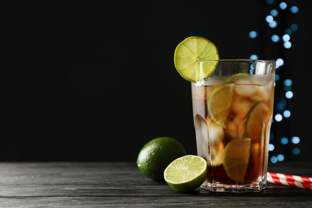 Glass of cold cola with citrus and ice on wooden table against dark background