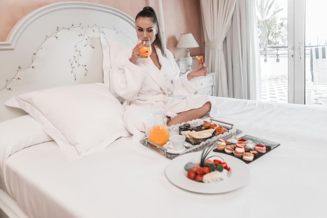 Woman drinking juice during breakfast on bed