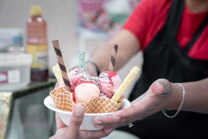 An adult Hispanic woman is serving a traditional Mexican ice cream with toppings to a client