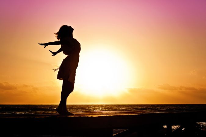 Silhouette of woman standing and opening her arms on beach during sunset