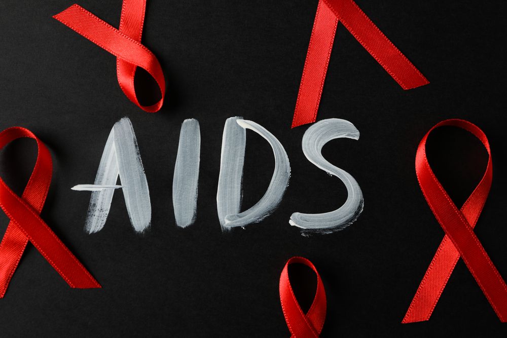 Red awareness ribbon and inscription AIDS on dark background, close up