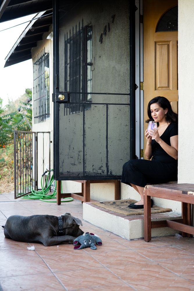 Woman holding glass of wine while sitting on front steps looking at her dog and smiling