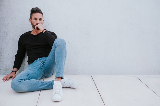 Adult stylish man sitting near grey wall