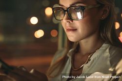 Close up of young woman wearing glasses using cellphone in office at night 4mdoW5