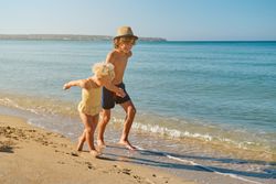 Happy smiling boy holding hand of little girl on beach and runni