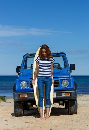 Woman leaning on big surfboard near car