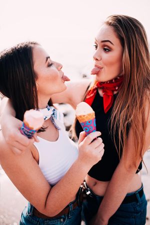 Two young women holding ice cream cones stick their tongues out at each other