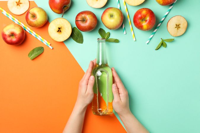 Female hands hold bottle of cider on two tone background. Composition with cider