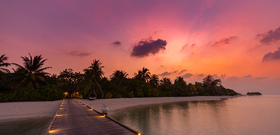 Wide shot of lit up walkway to a beach at a sunset