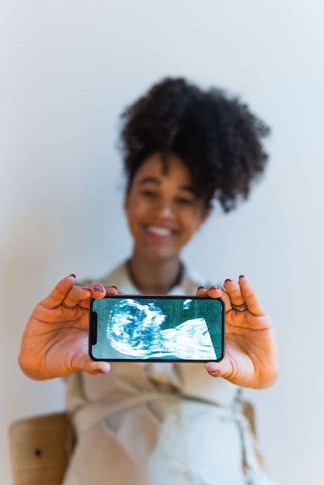 Smiling Black woman showing smartphone screen with baby ultrasound