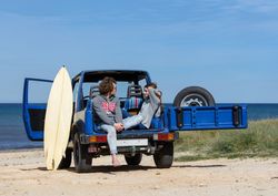 Couple with surfboard sitting on a car