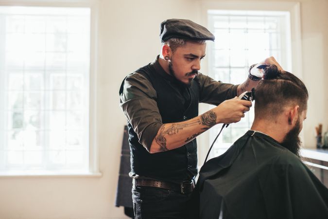 Stylish young barber trimming customer’s hair