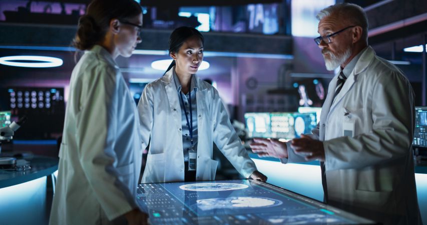 Modern Hospital Medical Research Center: Diverse Colleagues Gathered Around Interactive Touch Screen Table With CT Scans Of Brain On Display.