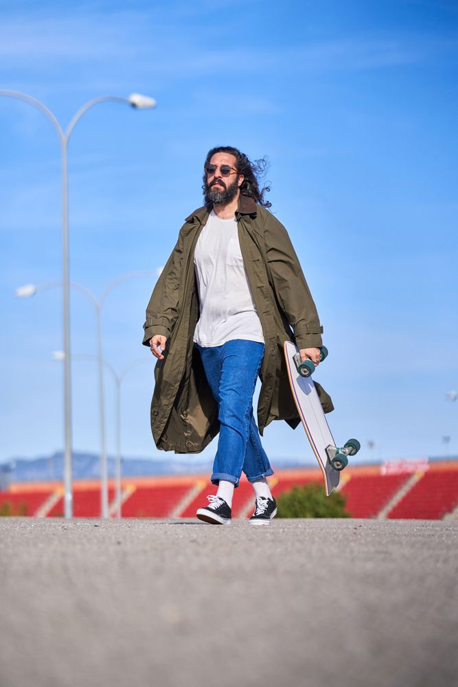 Trendy hipster man in raincoat walking with skateboard