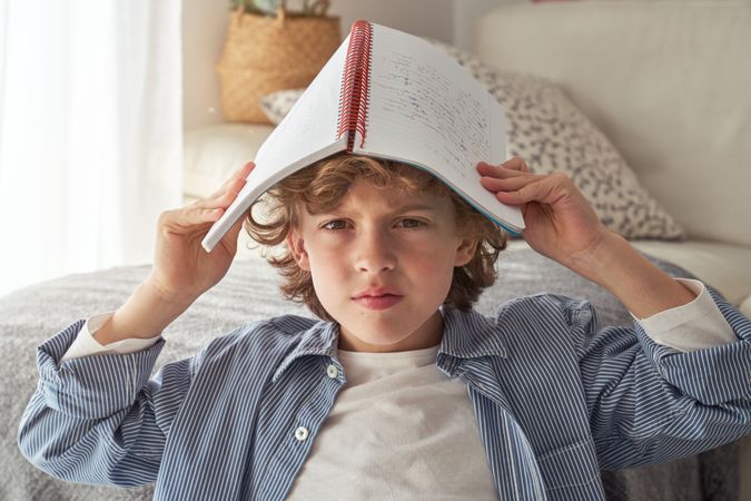 Grumpy boy covering head with copybook