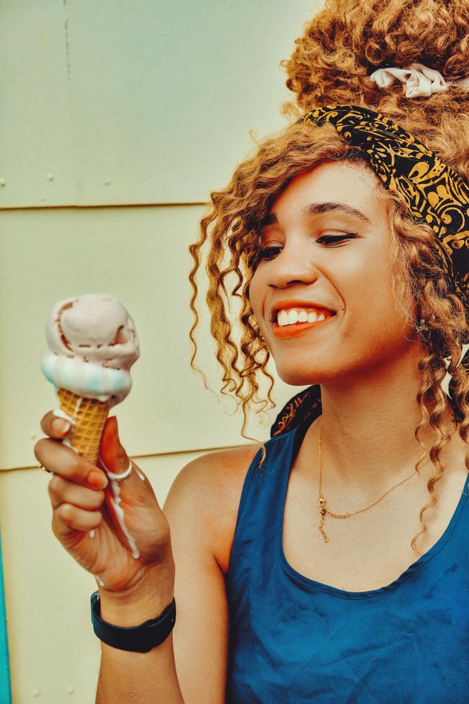 Vertical shot of smiling Black female enjoying an ice cream cone in the sun