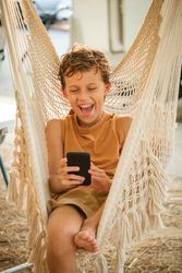 Boy with smartphone laughing at joke in hammock