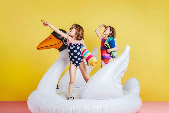 Twin girls having fun on inflatable toy flamingo over yellow background