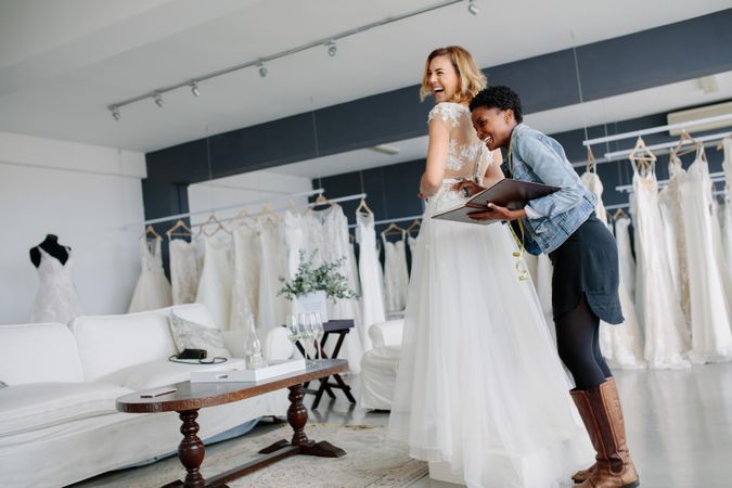 Female trying on wedding gown with women assistant in bridal wear shop