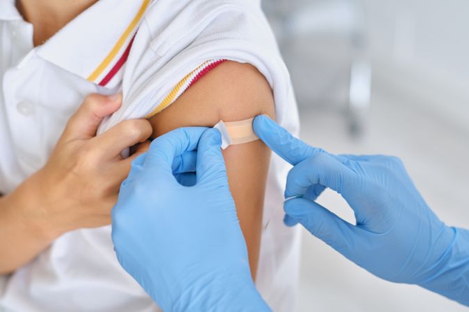 Crop doctor applying patch on shoulder of patient in clinic