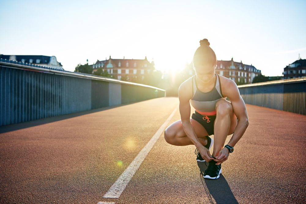 Fit woman leaning down to tie her shoes during her morning workout