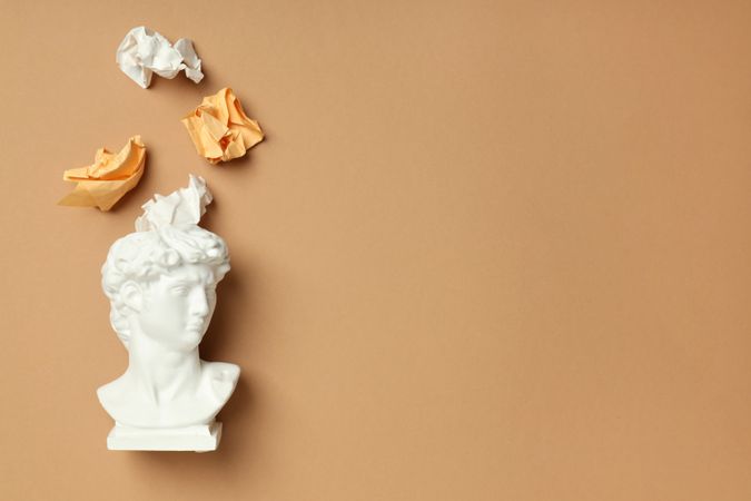 Marble bust with crumpled paper coming out of brain on brown background, copy space