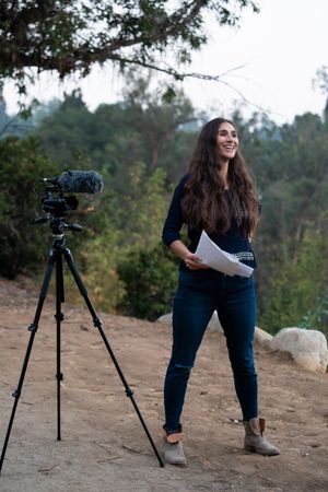 Female director standing confidently next to camera with script in hand