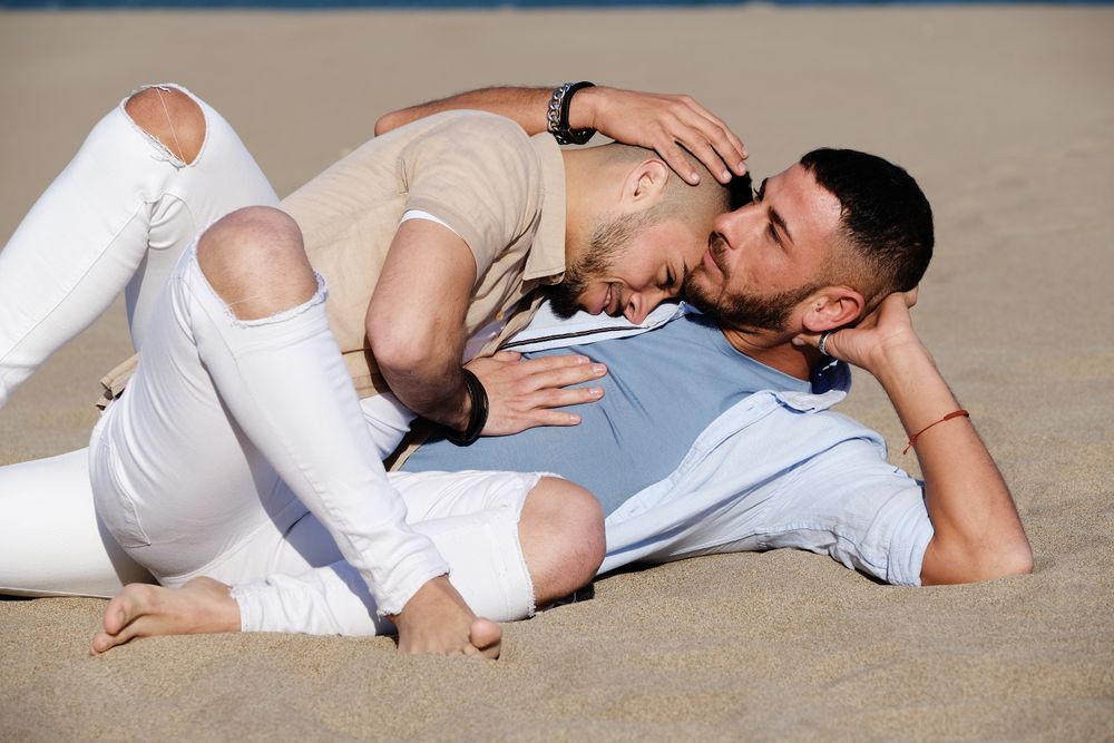 Affectionate gay couple relaxing on beach