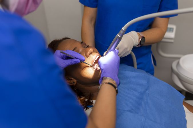 A Black female patient with dental hygienist checking gums and teeth