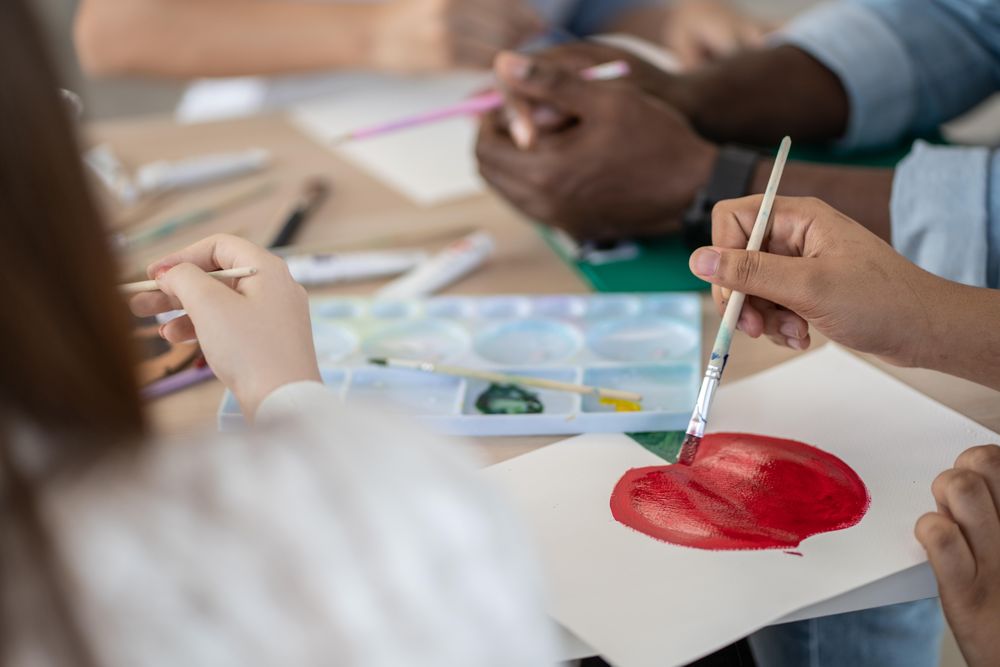 Close up of classroom table with students sitting painting a red apple