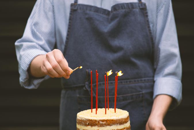 Man in blue apron lighting long candles on cake