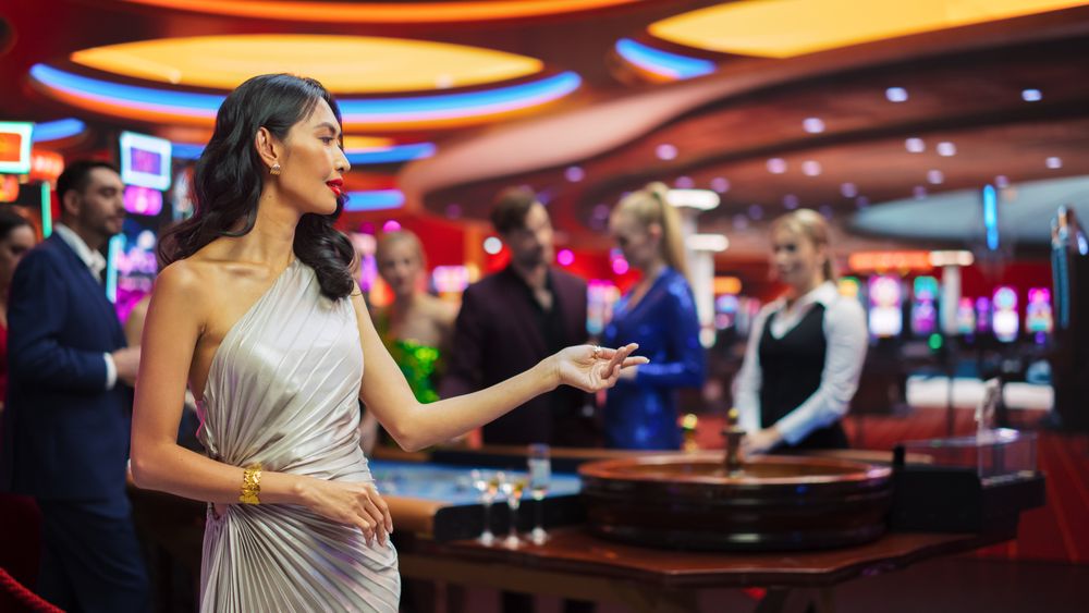 In a Modern Casino Building: Gorgeous Asian Woman Posing Confidently, Looking at Camera, Wearing a Fashionable Grey Dress.