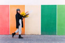 Woman with flowers walking against colorful wall