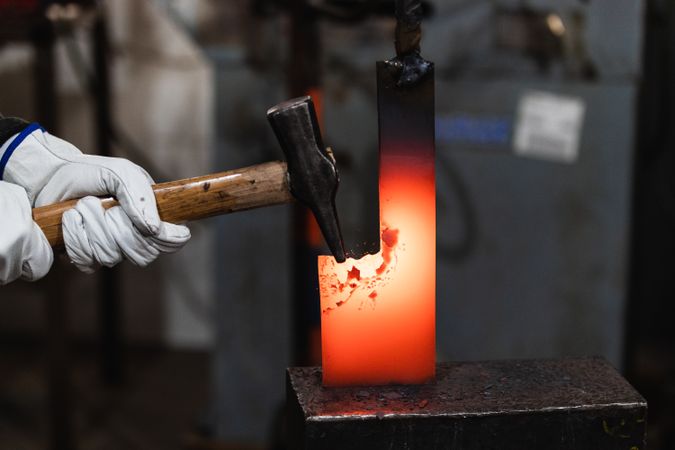 Blacksmiths forging hot metal with hammer in workshop
