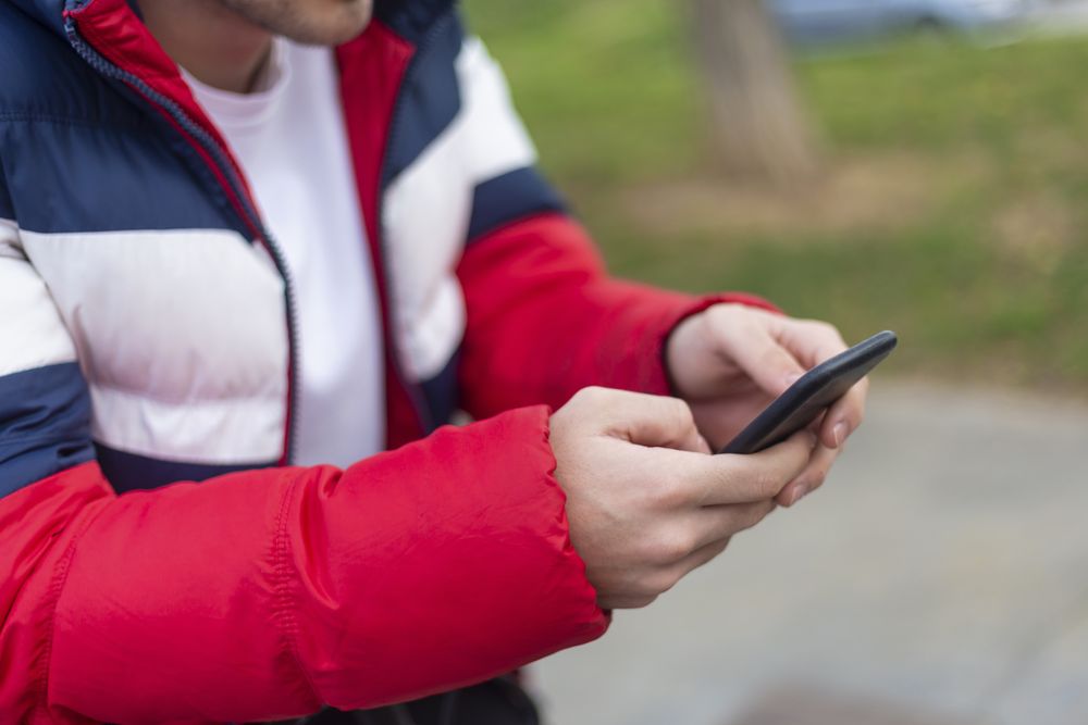 Hands of man with smartphone texting outdoors in the street