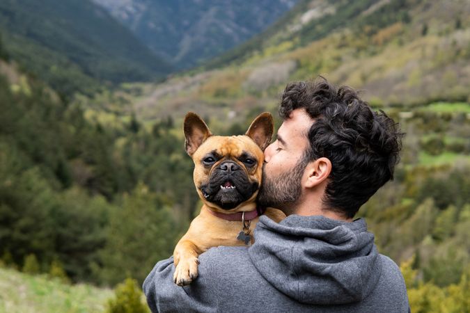Happy traveling man kissing cute dog in highlands