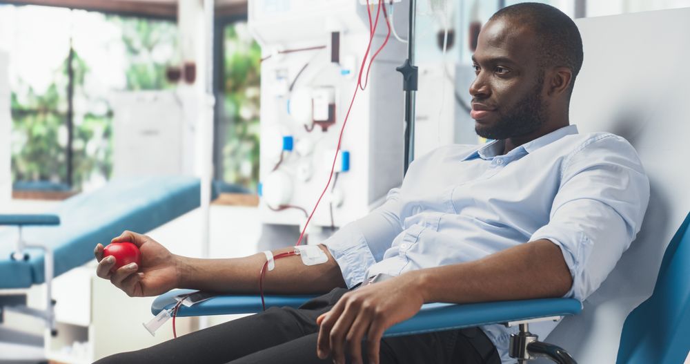 Male Donor Squeezing Heart-Shaped Red Ball To Pump Blood Through The Tubing Into Bag.